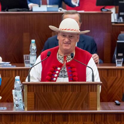 Mężczyzna w tradycyjnym stroju śląskim przemawia w sali posiedzeń, podczas Tygodnia Kultury Beskidzkiej. (wygenerowano przez AI)