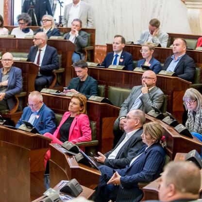 Sejmik Województwa Śląskiego podczas XV sesji, uczestnicy w strojach formalnych, siedzą w rzędach, słuchając przemówienia. (wygenerowano przez AI)