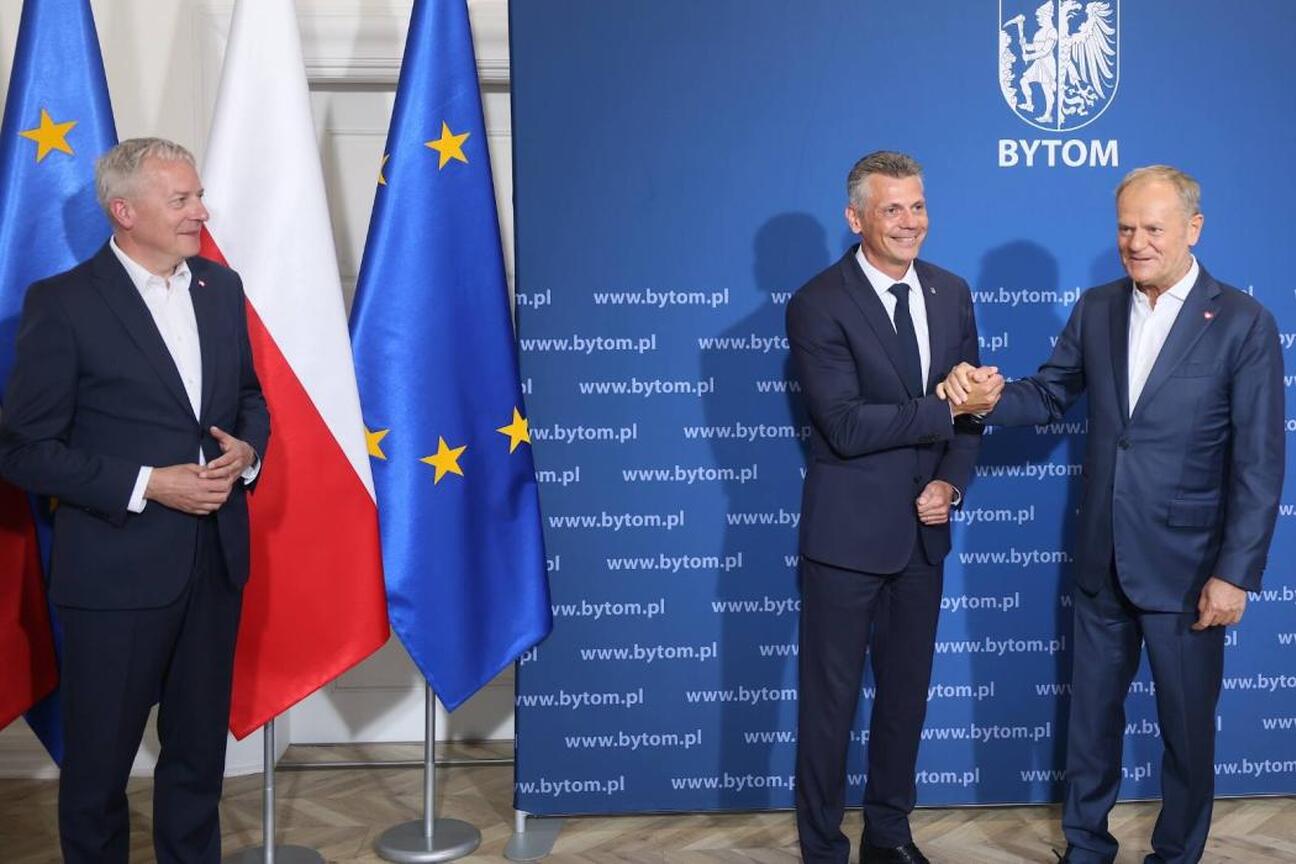 Grupa ludzi w garniturach bierze selfie, podczas spotkania z premierem Donaldem Tuskiem i innymi oficjali. (wygenerowano przez AI)