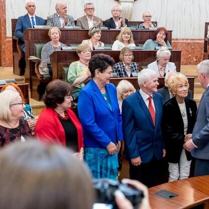Sylwetki seniorów uczestniczących w forum o Uniwersytetach Trzeciego Wieku w Sali Sejmu Śląskiego. (wygenerowano przez AI)