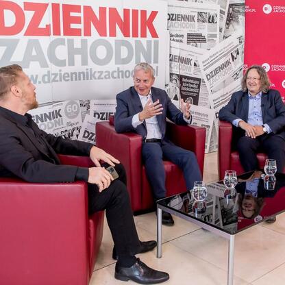 Trzech mężczyzn dyskutuje w czerwonych fotelach, przedstawiając koncepcję 