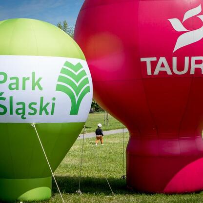 Dwa balony z logo TAURON i Parku Śląskiego na polu trawnym. (wygenerowano przez AI)