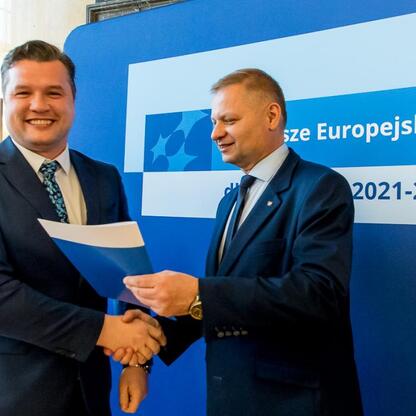 Członkowie Zarządu Województwa Śląskiego Rafał Adamczyk i Marcin Ryś wręczają listy gratulacyjne beneficjentom projektów edukacyjnych finansowanych z Europejskiego Funduszu Rozwoju Regionalnego. (wygenerowano przez AI)