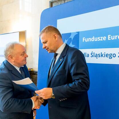 Członek Zarządu Województwa Śląskiego Rafał Adamczyk wręcza listy gratulacyjne beneficjentom projektów edukacyjnych finansowanych z Unii Europejskiej. (wygenerowano przez AI)