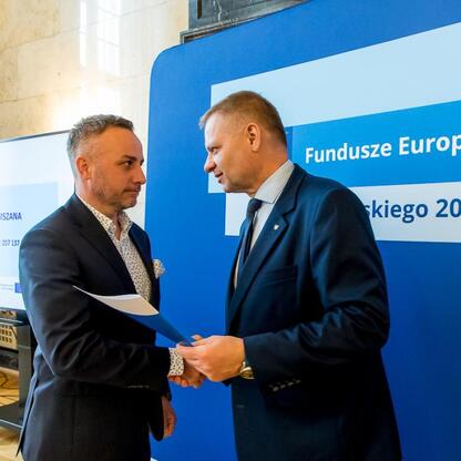 Członek Zarządu Województwa Śląskiego Rafał Adamczyk wręcza listy gratulacyjne beneficjentom projektów edukacyjnych finansowanych z Europejskich Funduszy. (wygenerowano przez AI)