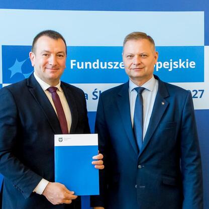 Członek Zarządu Województwa Śląskiego Rafał Adamczyk i jego współpracownik prezentują dokumenty z inwestycji w edukację w ramach Funduszy Europejskich dla Śląska 2021-2027. (wygenerowano przez AI)