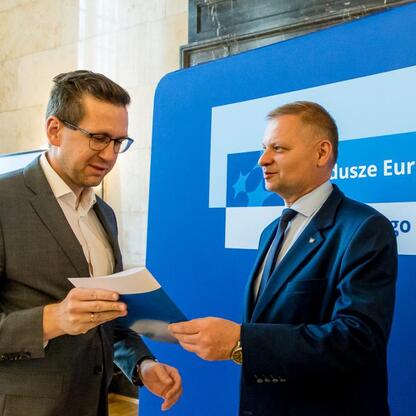 Członek Zarządu Województwa Śląskiego Rafał Adamczyk wręcza listy gratulacyjne beneficjentom programu Funduszy Europejskich dla Śląska 2021-2027. (wygenerowano przez AI)