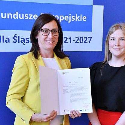 Joanna Bojczuk i Rafał Adamczyk wręczają listy gratulacyjne w ramach programu Fundusze Europejskie dla Śląska 2021-2027. (wygenerowano przez AI)