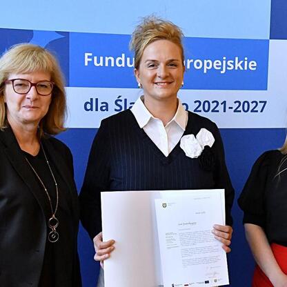 Trzy kobiety przedstawiają dokumenty, związane z Funduszami Europejskimi dla Śląska 2021-2027. (wygenerowano przez AI)