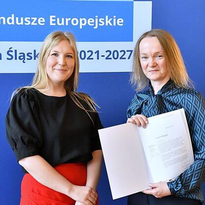 Joanna Bojczuk i Rafał Adamczyk wręczają listy gratulacyjne w ramach programu Fundusze Europejskie dla Śląska 2021-2027. (wygenerowano przez AI)