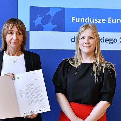 Joanna Bojczuk i Rafał Adamczyk wręczają listy gratulacyjne za dofinansowanie projektów edukacyjnych w ramach Funduszy Europejskich dla Śląska 2021-2027. (wygenerowano przez AI)