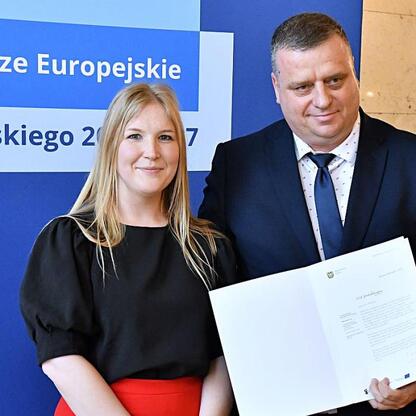 Joanna Bojczuk i Rafał Adamczyk wręczają listy gratulacyjne w ramach programu Fundusze Europejskie dla Śląska 2021-2027. (wygenerowano przez AI)