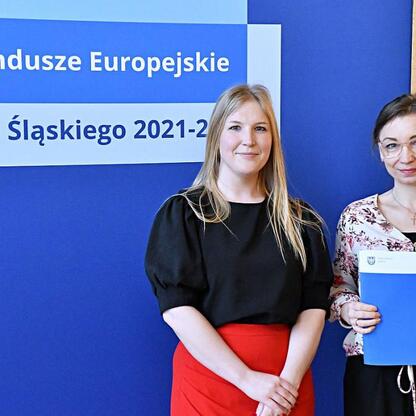 Joanna Bojczuk i Rafał Adamczyk prezentują listy gratulacyjne dla beneficjentów programu Fundusze Europejskie dla Śląska 2021-2027. (wygenerowano przez AI)