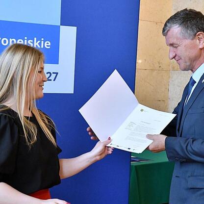 Joanna Bojczuk, Członkini Zarządu Województwa Śląskiego, wręcza dokument Rafałowi Adamczykowi, członkowi zarządu. Program Funduszy Europejskich dla Śląska 2021-2027. (wygenerowano przez AI)