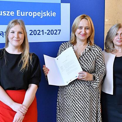 Trzy kobiety w strojach formalnych przedstawiają projekt finansowania edukacji w regionie Śląskim. (wygenerowano przez AI)