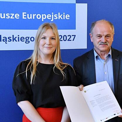 Joanna Bojczuk i Rafał Adamczyk prezentują listy gratulacyjne dla beneficjentów programu Fundusze Europejskie dla Śląska 2027. (wygenerowano przez AI)