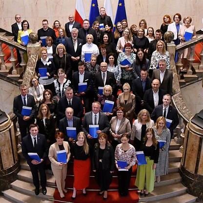 Grupa około 40 osób, prawdopodobnie urzędnicy lub beneficjenci, zgromadzona na grandowej schodach w formalnym uroczystości, związana z alokacją funduszy edukacyjnych dla Śląska. (wygenerowano przez AI)