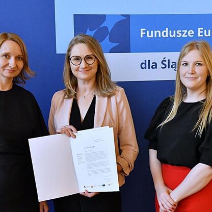 Trzy kobiety przedstawiają projekt Funduszy Europejskich dla Śląska 2021-2027. (wygenerowano przez AI)