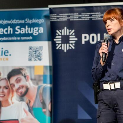 Na zdjęciu: Policjantka przemawia na konferencji o bezpieczeństwie drogowym i cyberbezpieczeństwie. (wygenerowano przez AI)