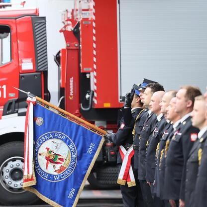 Ceremonia z okazji 15-lecia Komendy Miejskiej PSP w Częstochowie, gdzie strażacy w mundurach składają cześć czerwonej ciężarówce z numerem 