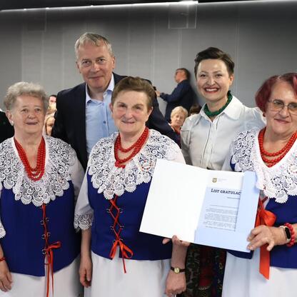 Grupa ludzi w tradycyjnych strojach uczestniczy w uroczystości w Śląskim Stadionie, otrzymując certyfikaty za wsparcie lokalnych tradycji. (wygenerowano przez AI)