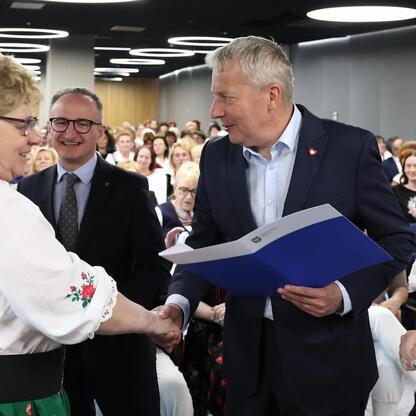 Wicemarszałek Grzegorz Boski i Marszałek Wojciech Saługa wręczają certyfikaty uczestnikom konkursu wspierania rozwoju kół gospodyń wiejskich w Śląskim Stadionie. (wygenerowano przez AI)