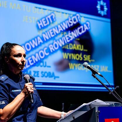 W Katowicach na spotkaniu z młodzieżą policjantka w mundurze prezentuje kampanię bezpieczeństwa i równości. (wygenerowano przez AI)