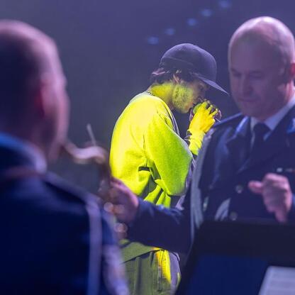 Na zdjęciu młody człowiek w żółtym stroju i czapce jest eskortowany przez policjanta na scenie podczas wydarzenia o bezpieczeństwie drogowym w Katowicach. (wygenerowano przez AI)