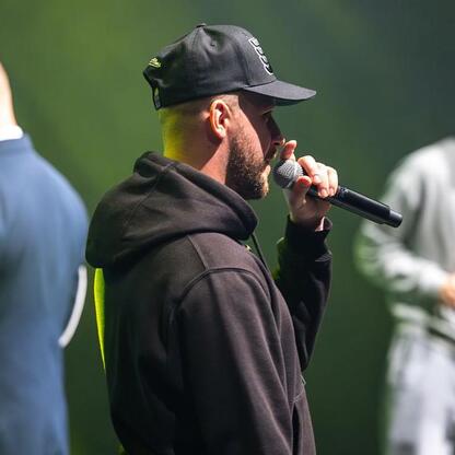 Mężczyzna w czapce i hoodie przemawia do publiczności, podczas spotkania o bezpieczeństwie drogowym i hejcie wśród młodzieży. (wygenerowano przez AI)
