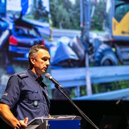 Policjant w mundurze, przemawiający na podium, podkreśla bezpieczeństwo drogowe i hejtu wśród młodzieży. (wygenerowano przez AI)
