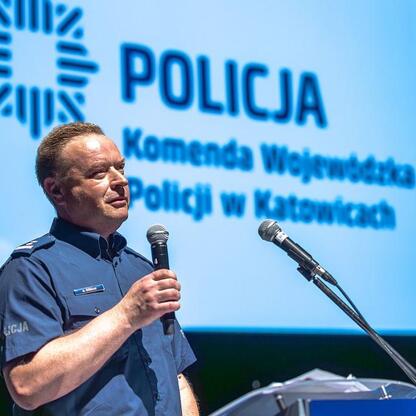 Policjant przemawia na podium w Katowicach, podczas kampanii o bezpieczeństwo drogowym. (wygenerowano przez AI)