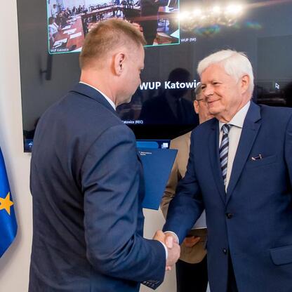 Dwóch mężczyzn w garniturach trzyma się za ręce, podczas inauguracji Wojewódzkiej Rady Rynku Pracy w Katowicach. (wygenerowano przez AI)