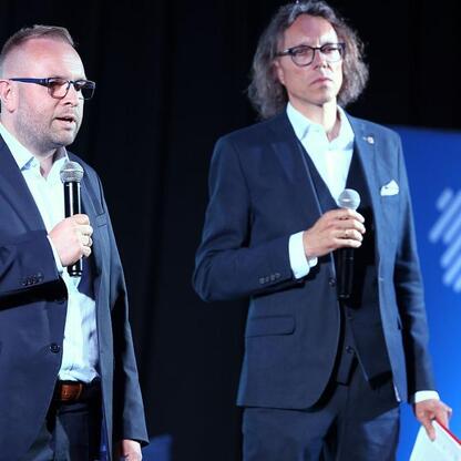 Dwa mężczyźni w garniturach prowadzą dyskusję na Business Mixer w Jaworznie, omawiając wyzwania gospodarcze regionu. (wygenerowano przez AI)