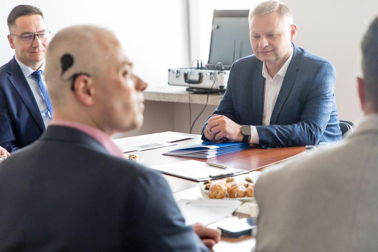 Rafał Adamczyk (Członek Zarządu Województwa) przekazuje dokument osobie z niepełnosprawnością podczas posiedzenia Wojewódzkiej Społecznej Rady ds. Osób Niepełnosprawnych. (wygenerowano przez AI)