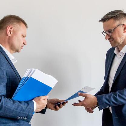 Rafał Adamczyk, Członek Zarządu Województwa Śląskiego, wręcza folder na posiedzeniu Wojewódzkiej Społecznej Rady ds. Osób Niepełnosprawnych. (wygenerowano przez AI)