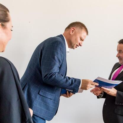 Rafał Adamczyk (Członek Zarządu Województwa) przekazuje dokument podczas posiedzenia Wojewódzkiej Społecznej Rady ds. Osób Niepełnosprawnych. (wygenerowano przez AI)