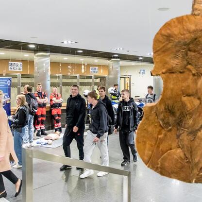 Wnętrze modernistycznego budynku, prawdopodobnie szkolnego lub centrum społecznego, z grupą młodych ludzi i dużym drewnianym rzeźbą w przedpolu. (wygenerowano przez AI)