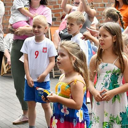 Zdjęcie przedstawia festiwal INDUSTRIADY, świętujące przemysłowe dziedzictwo Śląska. Uczestnicy w publicznym miejscu, dzieci w letniej odzieży, atmosfera relaksu. (wygenerowano przez AI)