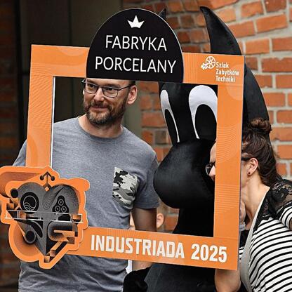 Fotografia przedstawia moment z festiwalu INDUSTRIADA w Fabryce Porcelany, gdzie ludzie interagują z fotobudką. (wygenerowano przez AI)