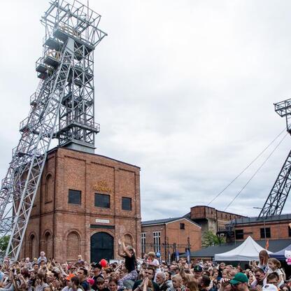 Fotografia przedstawia festiwal INDUSTRIADY w Zabytkowej Kopalni Ignacy w Rybniku, Polska. Wielka liczba ludzi cieszy się muzyką i atrakcjami festiwalowymi. (wygenerowano przez AI)