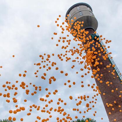 Widoczne na zdjęciu ujęcie festiwalu INDUSTRIADA, gdzie z wodnej wieży wolno lądują pomarańczowe balony, tworząc festynowy klimat. (wygenerowano przez AI)