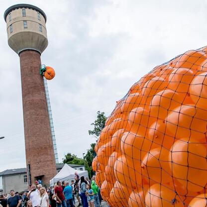 Widoczna jest atrakcyjna scena z festiwalu INDUSTRIADY, z dominującą pomarańczową rzeźbą i zgromadzoną publicznością. (wygenerowano przez AI)