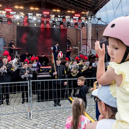 Ludzie cieszą się festiwalem INDUSTRIADY w Śląsku, gdzie młodzi i dorosli uczestniczą w koncertach i interaktywnych atrakcjach. (wygenerowano przez AI)