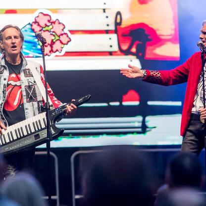 Fotografia przedstawia moment z festiwalu INDUSTRIADY, z dwoma artystami na scenie: pianistą i wokalistą, którzy wykonują muzykę dla publiczności. (wygenerowano przez AI)