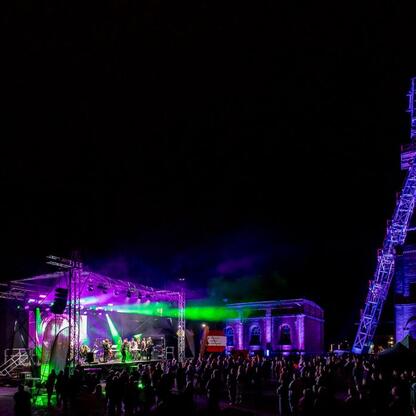 W nocy w Zabrzu, podczas festiwalu INDUSTRIADY, na scenie w Sztolni Królowa Luiza grają muzycy, a tłum zgromadzony podziwia ich koncert. (wygenerowano przez AI)
