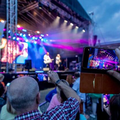 Fotografia przedstawiająca tłum widzów na festiwalu INDUSTRIADY w Silesia, z aktywnym uczestnikiem nagrywającym wydarzenie. (wygenerowano przez AI)