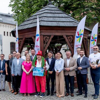 Grupa ludzi w formalnej odzieży przed tradycyjnym pawilonem na dziedzińcu zamkowym, podczas konferencji prasowej festiwalu Festiwal Górnej Odry. (wygenerowano przez AI)