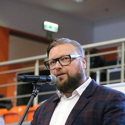 Mężczyzna w garniturze przemawia do mikrofonu na konferencji zdrowia w Bielsku-Białej. (wygenerowano przez AI)