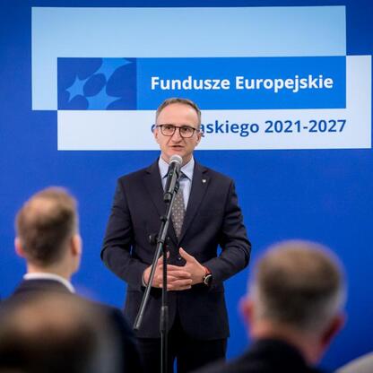 Wicemarszałek Województwa Śląskiego Grzegorz Boski przemawia na podium w Urzędzie Marszałkowskim, prezentując projekty finansowane z Europejskich Funduszy dla Śląska. (wygenerowano przez AI)