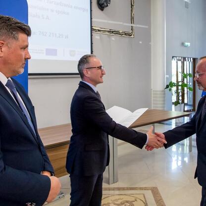 Trzech mężczyzn w strojach formalnych trzyma się za ręce w profesjonalnym środowisku, związany z energetyką i funduszami europejskimi. (wygenerowano przez AI)
